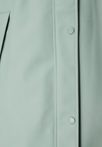 Lichtgroene waterdichte jackstof met glanzende textuur, voorzien van een sluitsysteem met knopen aan de voorkant, zichtbare stiksels en gladde panelen.