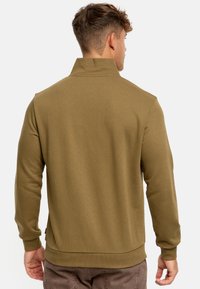 Chaqueta de pullover de color verde oliva, con canalé, de cuello alto, mangas largas y cintura ajustada. Tejido texturizado de color sólido.