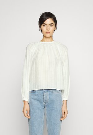 Blouse blanche texturée avec un col rond froncé et des manches longues, associée à un jean bleu taille haute. Design simple et léger.