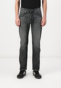 Donkergrijze jeans met een rechte pasvorm, vervaagde textuur, vijf zakken en zilverkleurige hardware. Gecombineerd met zwarte schoenen met witte strepen.