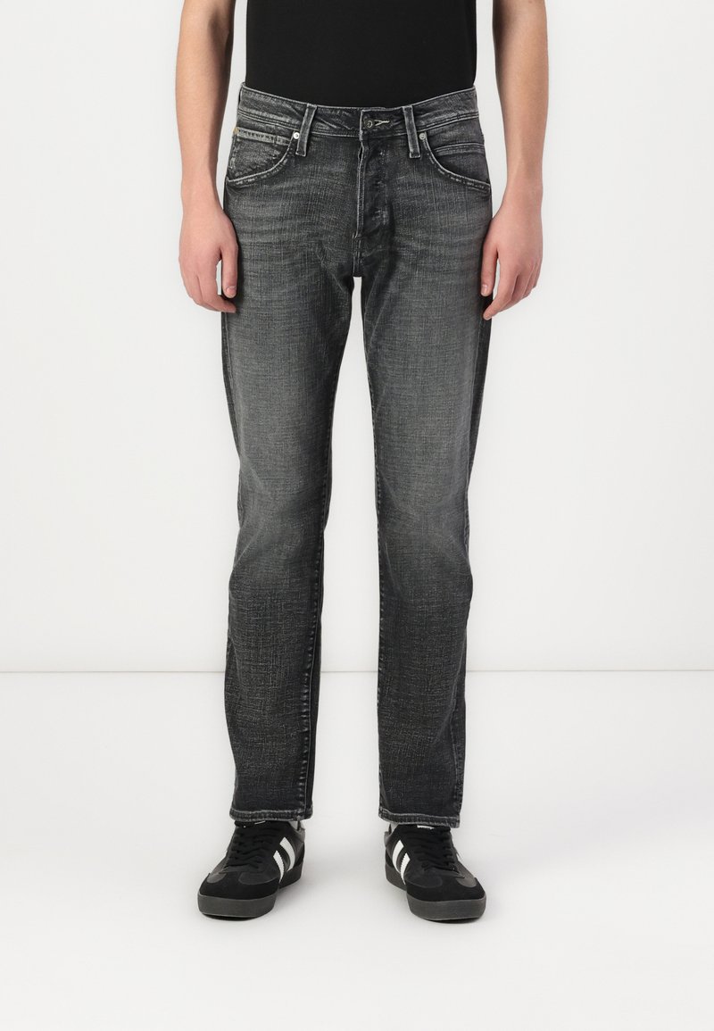 Donkergrijze jeans met een rechte pasvorm, vervaagde textuur, vijf zakken en zilverkleurige hardware. Gecombineerd met zwarte schoenen met witte strepen.