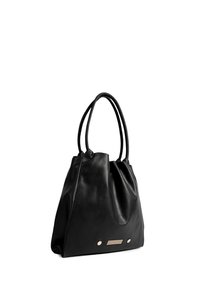 Zwarte leren tote bag met twee handvatten, zachte textuur, driehoekige vorm en metalen accenten aan de voorkant met een geprofileerde paneel.