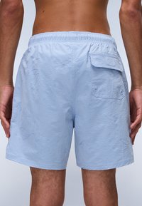 Shorturi de baie de culoare albastră deschisă cu un model texturat, talie elastică și buzunar lateral. Materialul pare ușor și cu uscare rapidă.