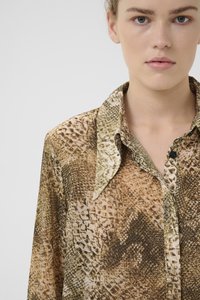 Camicia in stampa serpente marrone e beige con colletto a punta, chiusura con bottoni e superficie testurizzata. Il tessuto ha un aspetto liscio e lucido.