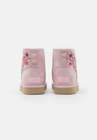 Botines de ante rosa con bordados florales, un forro interior suave y una suela de goma marrón. Etiqueta de logo en el talón.