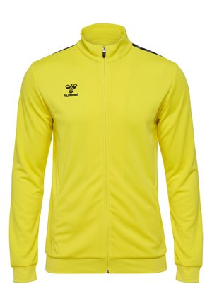 Gul sportsjakke med høj krave, lynlås fortil, sorte skulderaccenter, struktureret stof og Hummel-logo på venstre bryst.