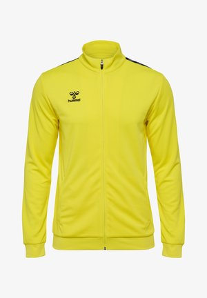 Gul sportsjakke med høj krave, lynlås fortil, sorte skulderaccenter, struktureret stof og Hummel-logo på venstre bryst.
