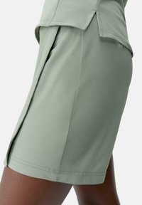 Primer plano de una persona que lleva pantalones cortos verde claro y una camiseta a juego con un detalle de abertura lateral en ambas prendas.