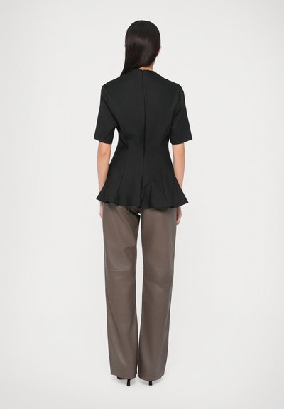 Top negru cu peplum, cu mâneci scurte și fermoar la spate, asortat cu pantaloni larga maro dintr-un material neted și strălucitor.