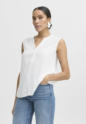 White sleeveless blouse with a henley neckline, textured fabric, and three buttons at the front. Paired with blue jeans.