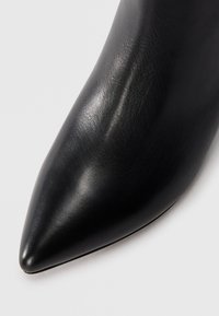 Scarpa con tacco alto di pelle nera a punta, con una texture liscia e un design elegante, caratterizzata da una silhouette snella e una finitura lucida.
