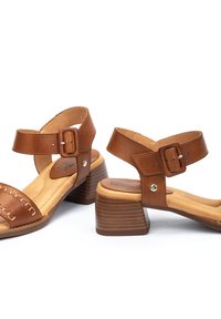 Sandalias de cuero marrón con tacón de bloque, que cuentan con una amplia correa para el tobillo con hebilla, detalle de costura en la correa del dedo del pie y suela texturizada.