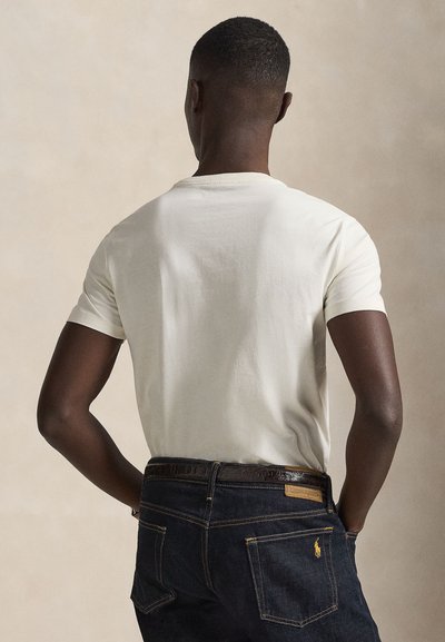 T-shirt blanc en coton avec un col rond, des manches courtes et une coupe décontractée, associé à un jean en denim foncé avec des coutures jaunes et un écusson logo.