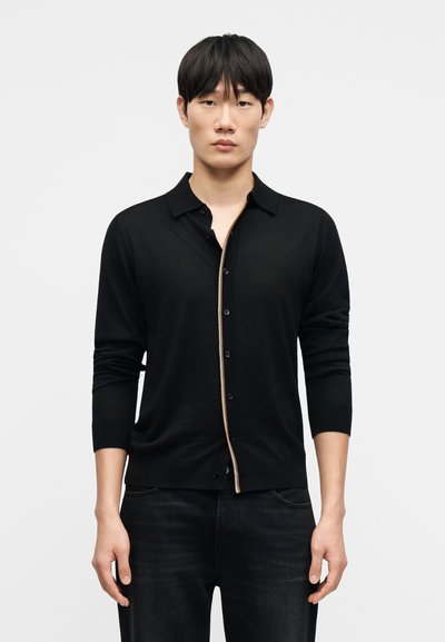 Cardigan noir avec fermeture boutonnée complète, manches longues, col et bordure arc-en-ciel contrastante le long de la patte de boutonnage. Texture en maille douce.
