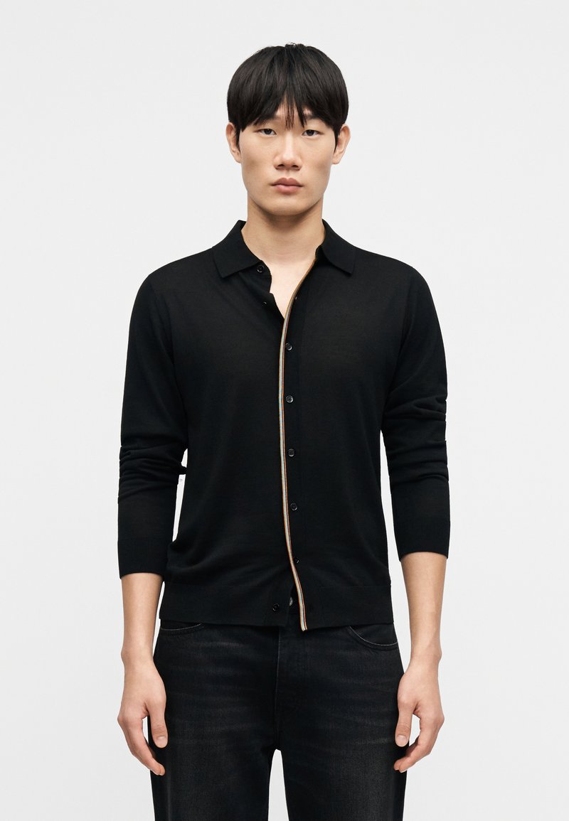 Μαύρο ζακέτα με πλήρη κούμπωμα με κουμπιά, μακριά μανίκια, γιακά και αντίθετο πολύχρωμο περιθώριο με ουράνιο τόξο κατά μήκος της πλάκας. Μαλακή πλεκτή υφή.