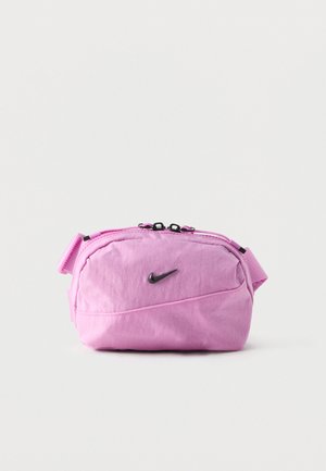 Sac banane Nike rose avec logo Swoosh noir, compartiment principal zippé et sangle réglable sur fond blanc uni.