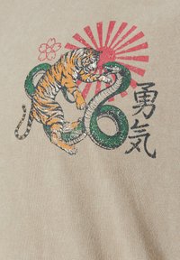 Tigre et serpent vert enfermés dans un combat avec un soleil rouge levant, fleurs de cerisier et caractères japonais noirs sur tissu beige.