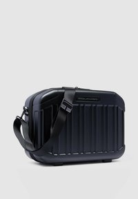 Zwarte harde reistas met geribbelde structuur, verstelbare riem en logo-accent. Afgeronde vorm en ritssluiting voor veilige toegang.