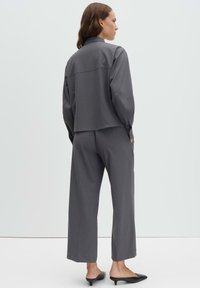 Veste grise sur mesure et pantalons à jambes larges, tous deux en tissu texturé. La tenue présente une coupe décontractée et des détails de design minimalistes.