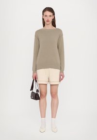 Lys beige strikket genser med rund hals, kombinert med kremfargede shorts, hvite sokker, og en liten mørk håndveske.