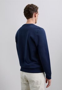 Sudadera de algodón azul marino con mangas largas, puños y dobladillo acanalados, y un cuello redondo. Parece suave con un diseño simple y limpio.