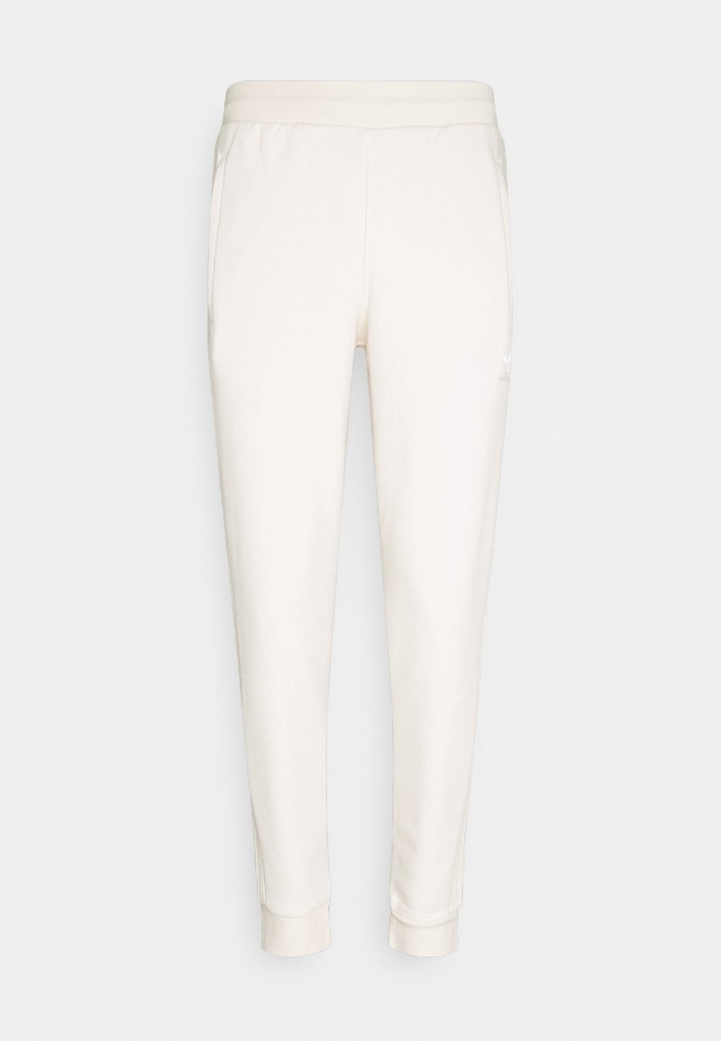Pantalon de jogging couleur crème en tissu doux. Il présente un design fuselé, une taille élastique, deux poches latérales et un petit logo.