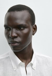 Close-up of a person wearing a white linen shirt with button-down collar. Smooth skin texture, short hair, neutral background.