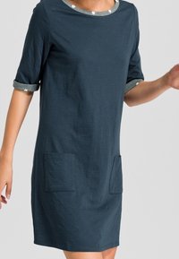 Robe T-shirt bleu marine en tissu doux, avec des manches roulées ornées de pois et deux poches plaquées à l'avant.