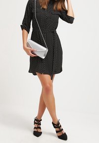 Černé šaty s puntíky, s páskem v pase, krátkými rukávy a vyhlazenou sukní. V kombinaci se stříbrnou psaníčkem a černými botami na šněrování.