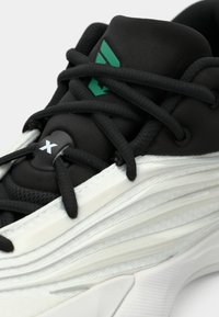 Kratak prikaz crno-bijelog tenisica s debelim crnim vezicama, zelenim logotipom na jeziku i teksturiranim slojevitim dizajnom potplata.