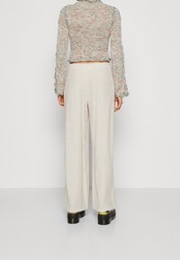 Lehké, krémové kalhoty s širokými nohavicemi z měkkého materiálu, spárované s texturovaným, vícebarevným pleteným topem s třásněmi.
