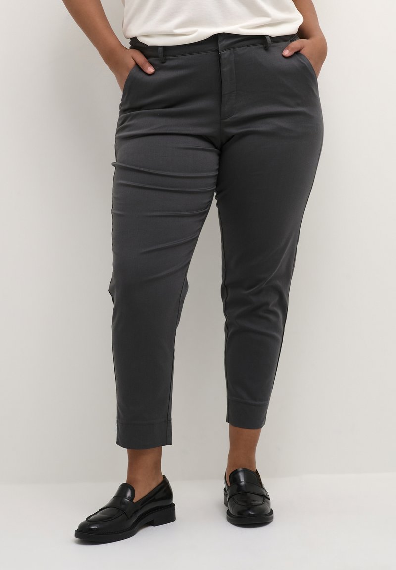 Pantalon gris foncé sur mesure, coupe slim, avec une texture lisse, des passants de ceinture et une jambe raccourcie, associé à des mocassins noirs.
