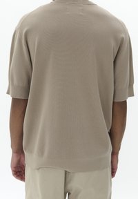 Béžový pletený svetr s krátkým rukávem a volným střihem, žebrovaným výstřihem a lemem, hladkou strukturou a subtilními švy na zadní straně.