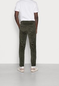 Olivgrön manchesterbyxor med slim fit, två bakfickor och textil med struktur. Kombineras med vit t-shirt och ljusa skor.