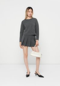 Grå croppet genser, grå plisserte mini skjørt, svarte spisse hæler og en hvit håndveske. Teksturert stoff og enkel design.