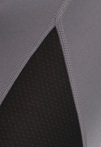 Zbliżenie na szare i czarne panele materiałowe z wzmocnionymi szwami i małymi perforacjami w czarnej części.