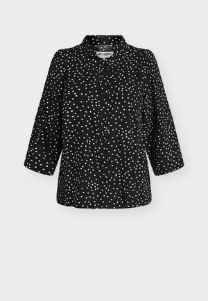 Mustast nööpidega pluus valgete ebaühtlaste täppidega, kolmeveerandvarrukatega ja klassikalise kraega, esitatud lihtsal taustal.