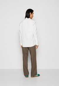 Witte langslavenshirt met een puntige kraag, gecombineerd met bruine wijde broek en groene sneakers met witte strepen.