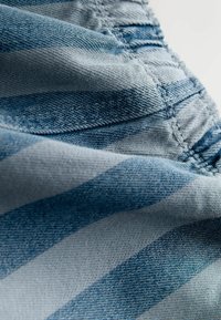 Denimstof med et blåt og gråt stribet mønster og synlig syning. Materialet ser blødt ud med en struktureret overflade.