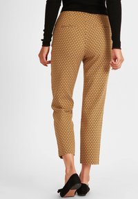 Pantalons ajustés en tissu à motifs dorés, avec une longueur crop et une taille élastique, assortis à des chaussures noires.