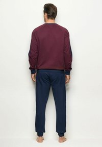 Sudadera burdeos de manga larga con detalles en azul marino, combinada con pantalones de chándal azul marino. Tejido liso, corte relajado, puños y dobladillo acanalados.