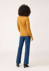 Musztardowy dziany sweter o fakturze w jodełkę, zestawiony z ciemnoniebieskimi rozkloszowanymi dżinsami i czarnymi botkami na obcasie.