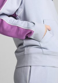 Felpa azzurra con una manica viola, caratterizzata da dettagli di cucitura e una tasca frontale. Tessuto morbido con una vestibilità comoda e polsini a coste.