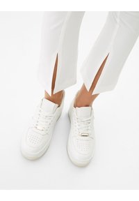 Vita snörskor i spets med perforerat tåparti, stoppad krage och detaljer i guld, tillsammans med vita byxor med sidsprund.