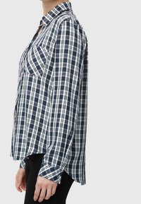 Camicia a quadri navy e bianca con colletto e tasche frontali, dotata di maniche lunghe e vestibilità rilassata. Tessuto di cotone morbido.