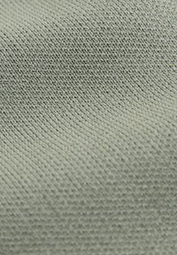 Tissu texturé de couleur verte douce, présentant un motif fin tissé avec une surface lisse et une légère élasticité.