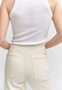 Top de tirantes blanco acanalado combinado con pantalones de tiro alto de color crema que cuentan con dos bolsillos traseros y una textura suave.