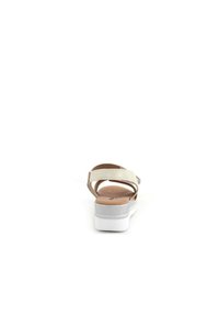 Sandal beige con una fascia larga, vista posteriore. Presenta una soletta imbottita e una suola bianca con un accento argento. Design piatto.