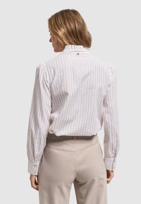 Biała bluzka w paski z falbaną przy kołnierzyku, bufiastymi rękawami i zapięciem na guziki przy mankietach. Połączona z beżowymi spodniami o wysokim stanie.