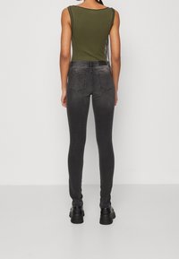 Svart smala jeans med en blekt finish, två bakfickor och midjehög linning, i kombination med en mörkgrön ribbad linne.